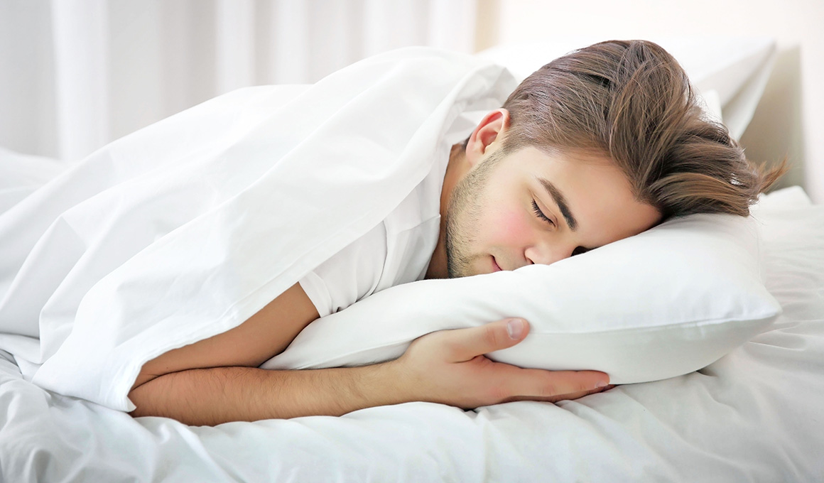 Junger Bauchschläfer mit braunen Haaren schläft auf seinem Kissen.