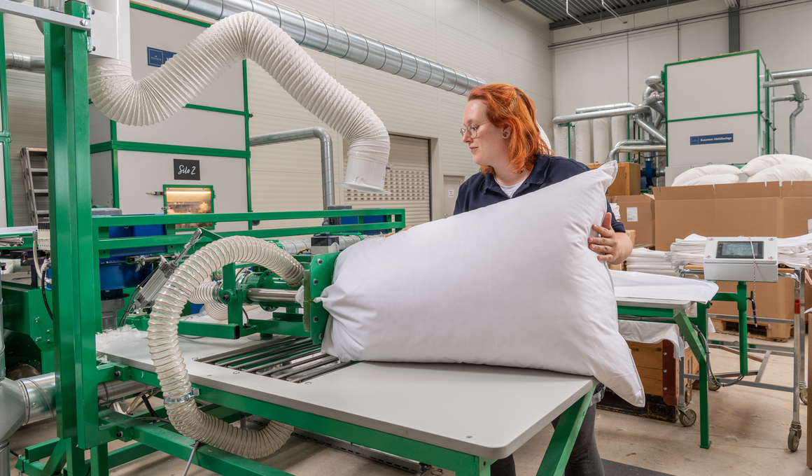 Mitarbeiterin bei der maschinellen Verarbeitung eines Kissens in der Bettwarenproduktion – Symbol für hygienische Fertigung und milbenfreie Schlafprodukte.