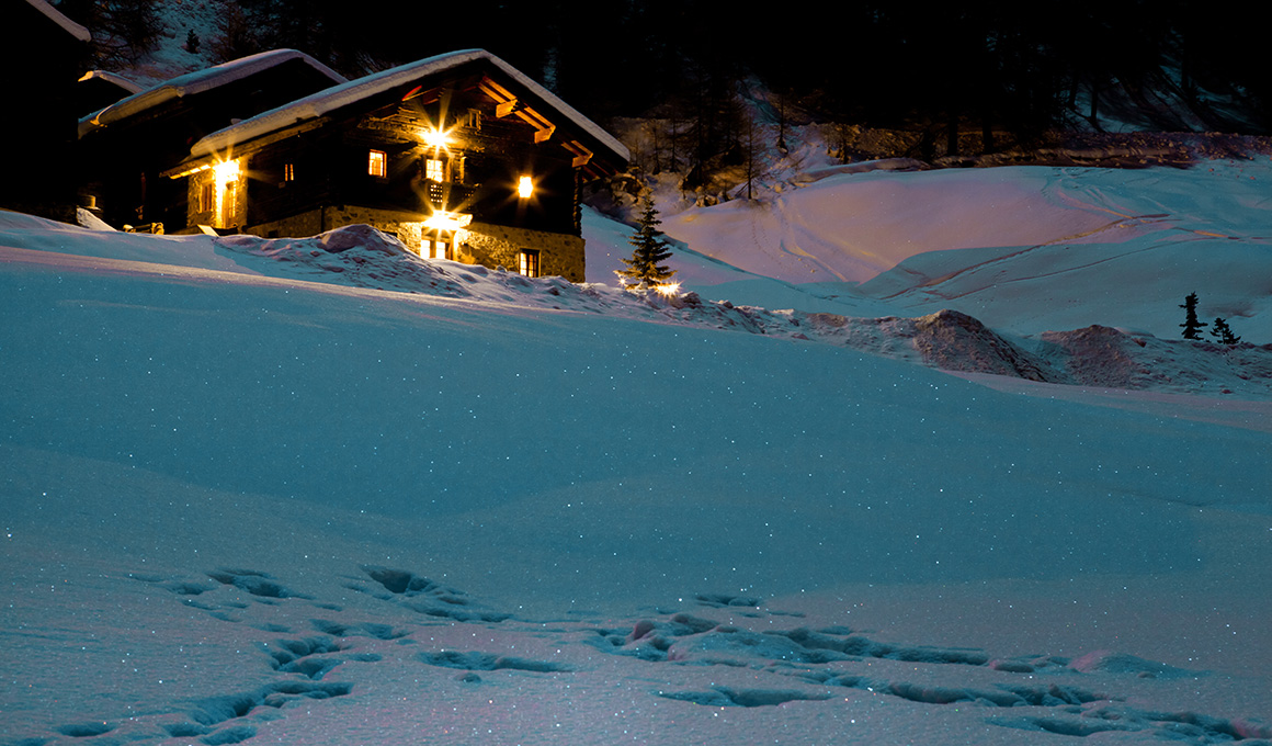 Gemütlich beleuchtetes Chalet in verschneiter Winterlandschaft – Symbol für wohlige Wärme und optimalen Schlafkomfort mit den saisonal passenden Duvets von billerbeck.