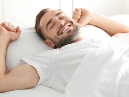 Mann im weissen T-Shirt streckt sich im Bett.