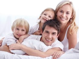 Lächelnde Familie im Bett – Symbol für erholsamen Schlaf und gesundes Leben durch passende Duvets und ergonomische Kissen.