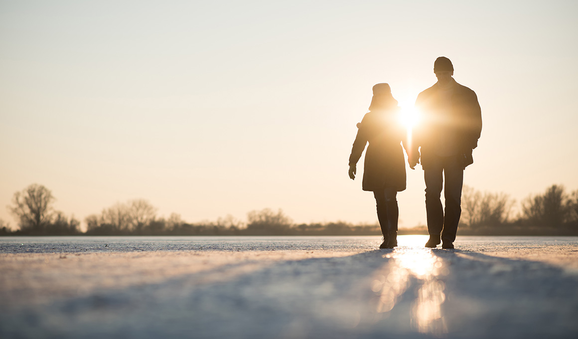 Paar spaziert bei Sonnenuntergang im Winter – Symbolbild für gesunde Routinen, frische Luft und Tageslicht als Hilfen zur Anpassung an die Winterzeitumstellung.