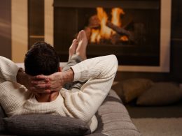 Mann liegt auf dem Sofa und wärmt seine Füsse vor dem Kamin.