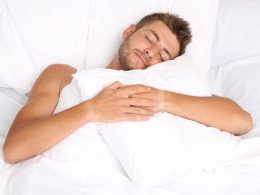 Man liegt zugedeckt in seinem Bett und hält sein Kissen umarmt.