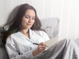 Frau mit schwarzen Haaren liegt im Bett mit ihrem Notizbuch in der Hand.
