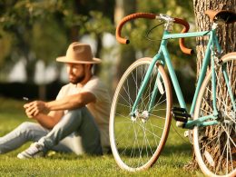 Man mit einem Hut macht nach einer Fahrradfahrt eine Pause auf einer grünen Wiese.