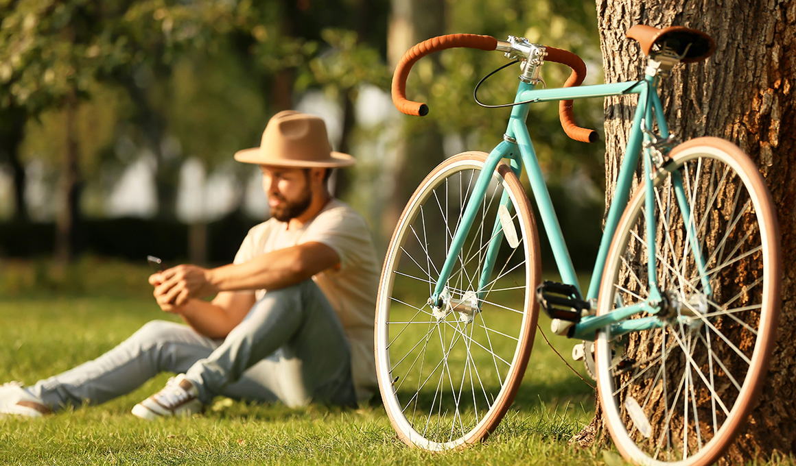 Man mit einem Hut macht nach einer Fahrradfahrt eine Pause auf einer grünen Wiese.