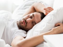 Mann mit kurzen, schwarzen Haaren in weissem T-Shirt schläft auf in seinem Bett