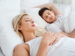 Frau mit blonden Haaren und Mann mit dunklen Haaren schlafen gemeinsam im Bett und sind zugedeckt mit zwei separaten Duvets.