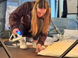 Eine Mitarbeiterin der billerbeck Schweiz AG kniet am Boden und zupft an der Ecke eines Daunen-Duvets. In der anderen Hand hält sie ein Bügeleisen.