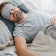 Ein Mann trägt eine Schlafmaske über den Augen und schläft ruhig im Bett.
