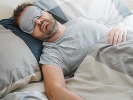 Ein Mann trägt eine Schlafmaske über den Augen und schläft ruhig im Bett.