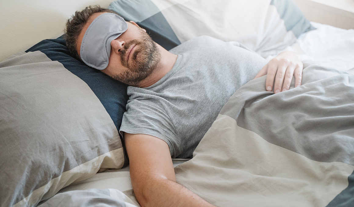 Ein Mann trägt eine Schlafmaske über den Augen und schläft ruhig im Bett.