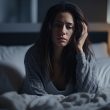 Frau sitzt nachts wach im Bett. Sie wirkt gestresst und müde.