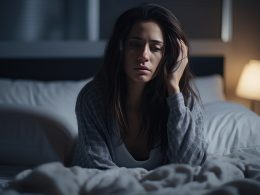 Frau sitzt nachts wach im Bett. Sie wirkt gestresst und müde.